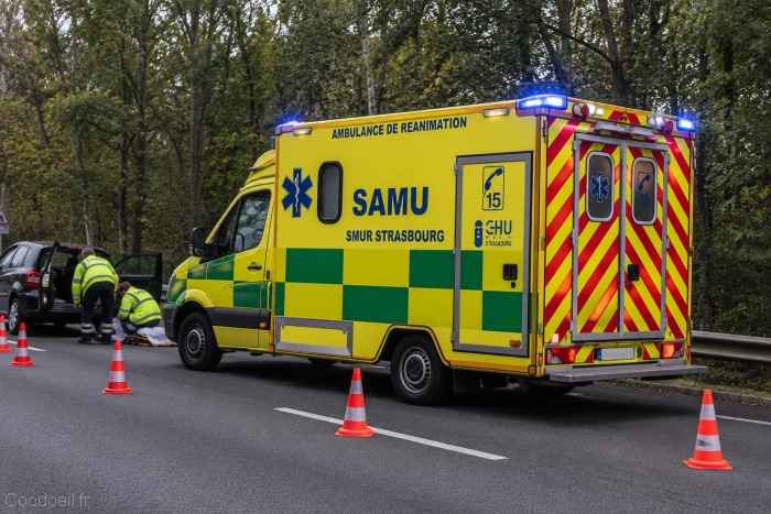 Nouvelle ambulance SAMU/SMUR aux couleurs nationales lors d'une intervention routière Illustration hyperréaliste d'une ambulance de réanimation du SAMU/SMUR Strasbourg conforme aux nouvelles recommandations nationales de signalétique. Le véhicule, revêtu d'une carrosserie jaune fluorescent avec damiers verts, intervient sur un accident de la route. Cette nouvelle identité visuelle vise à harmoniser les véhicules médicaux d'urgence sur l'ensemble du territoire français et à renforcer leur visibilité auprès des automobilistes.