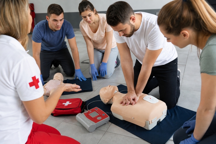 Participants en formation PSC1 r&eacute;alisant une r&eacute;animation cardio-pulmonaire sur mannequin avec utilisation d&rsquo;un d&eacute;fibrillateur sous la supervision d&rsquo;un formateur.