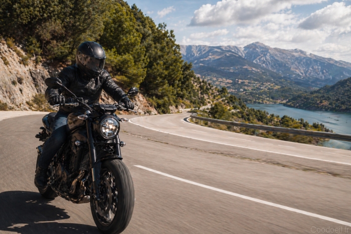 Motard &eacute;quip&eacute; roulant sur une route sinueuse en montagne avec vue sur un lac et des paysages naturels, illustrant la libert&eacute; et la passion de la moto.